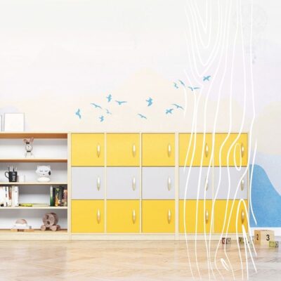 Żółte i szare szafki do szatni sportowej stoją obok półki z zabawkami i książkami na tle pastelowej ściany z dekoracją w postaci ptaków.